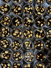 Load image into Gallery viewer, Overhead view of several rows of open jars of pickled black garlic