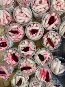 Overhead view of several rows of open jars of pickled turnip with a piece of red beet for color